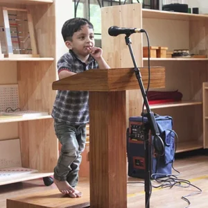 a young boy standing at a podium in front of a microphone – Mont Ivy Preschools