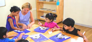 a Montessori teacher sitting at a table surrounded by children – Mont Ivy Preschools